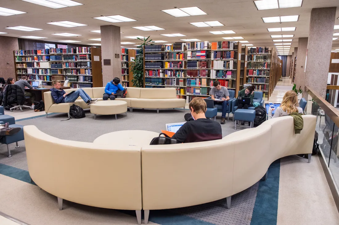 Students sitting on a large couch studying in a library.