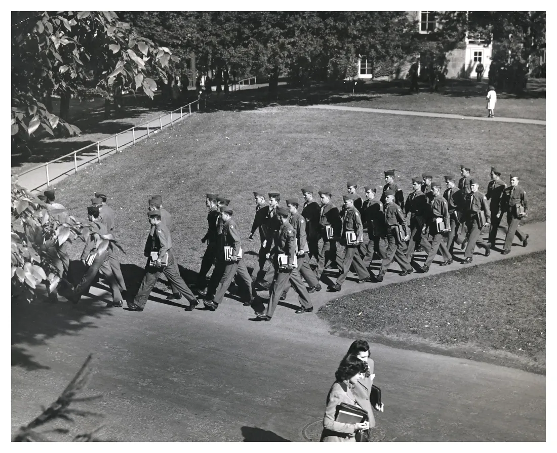 In an archival photo dating to WWII era, a group of soldiers walk across campus.