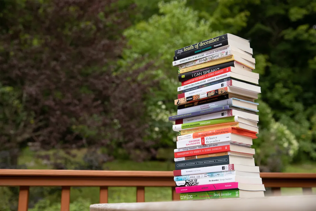 Stack of books on a table outside, with trees as a backdrop.
