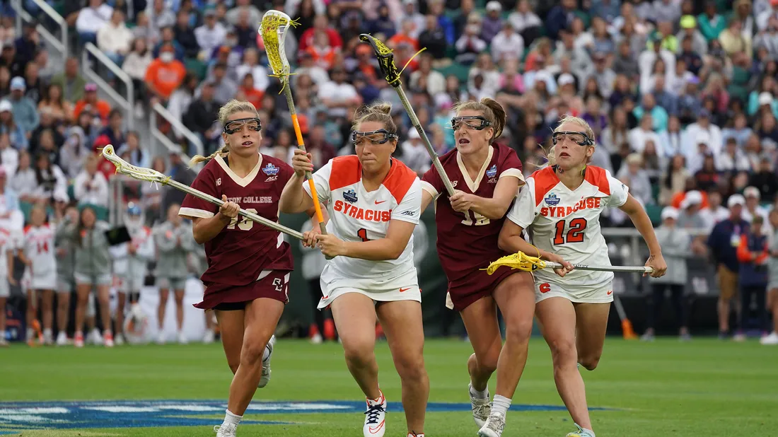 Four women battling out on lacrosse field at national championship game.