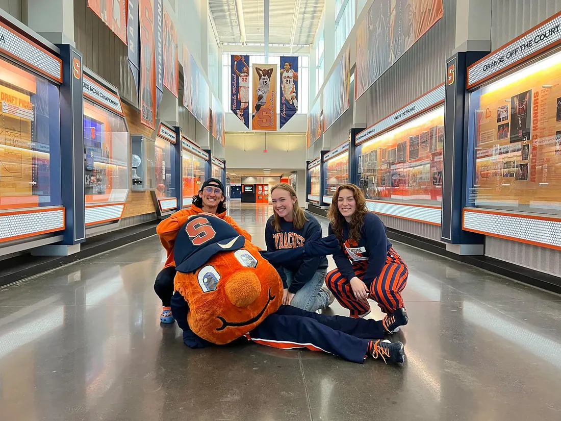 Three students and the mascot Otto in a hallway.