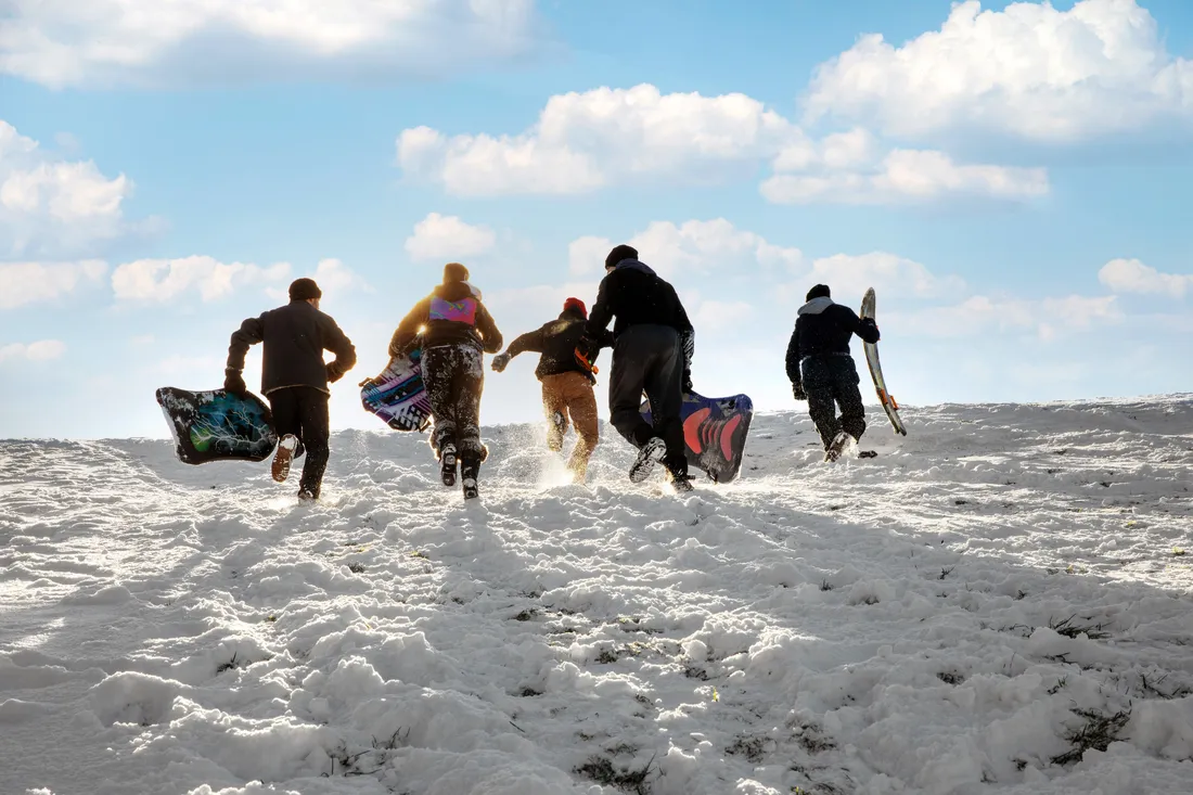 People running uphill with sleds in the winter.