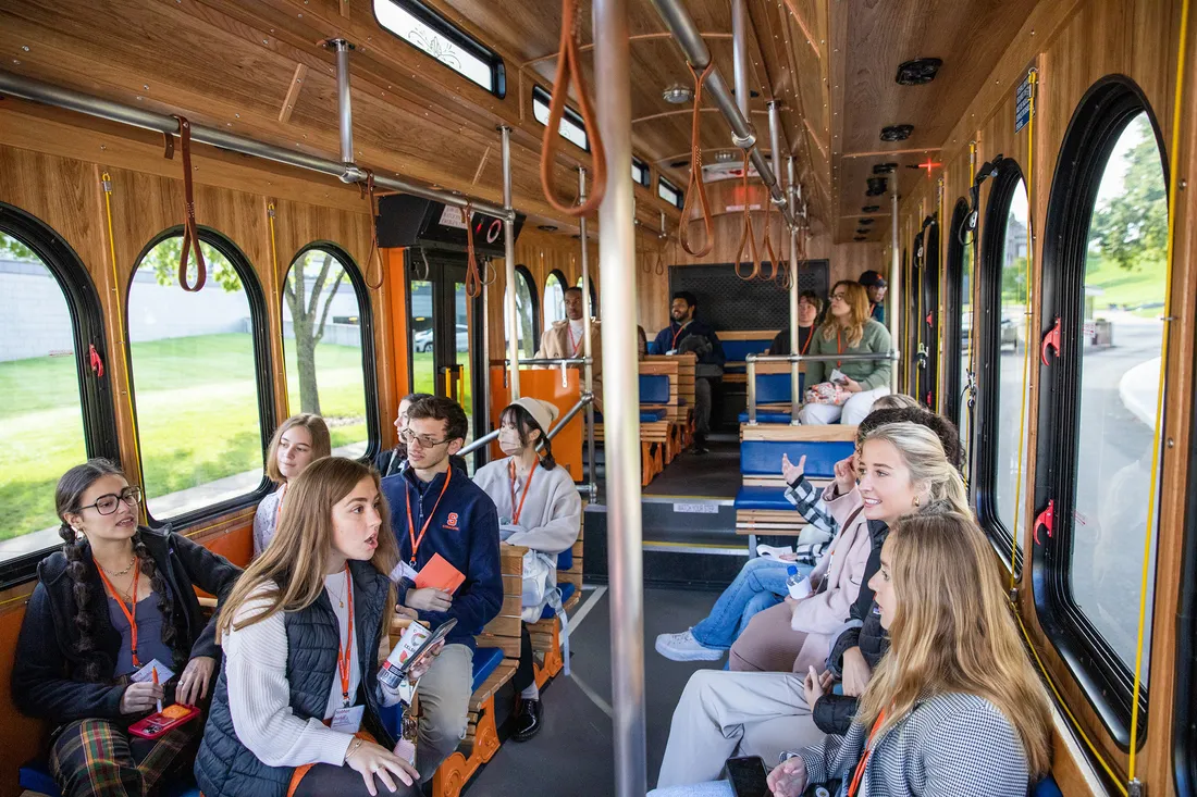 Photo of students sitting on a trolley chatting with one another.