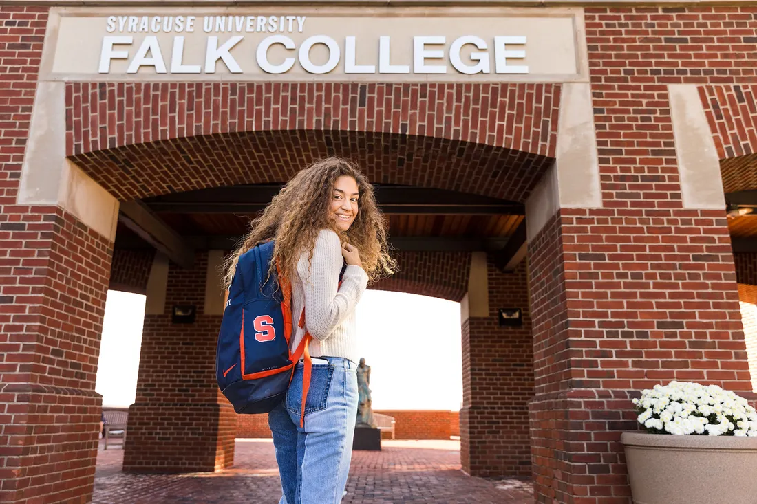 Student standing and smiling outside of Falk College.