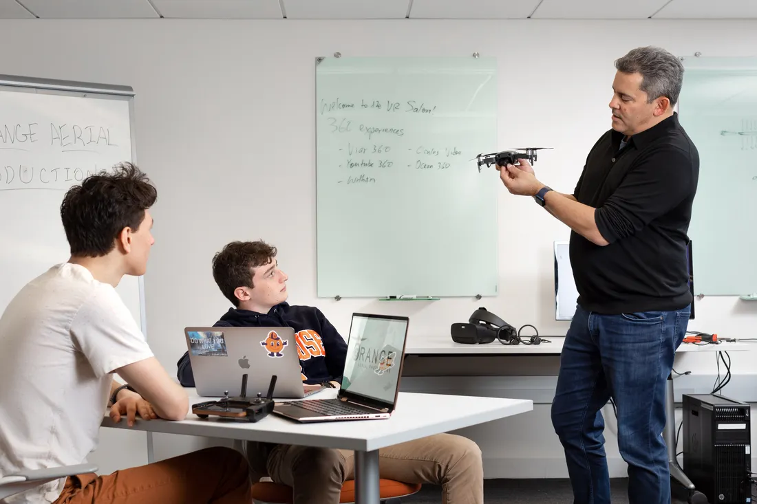 Professor Dan Pacheco working with students in class, holding a drone in his hands.
