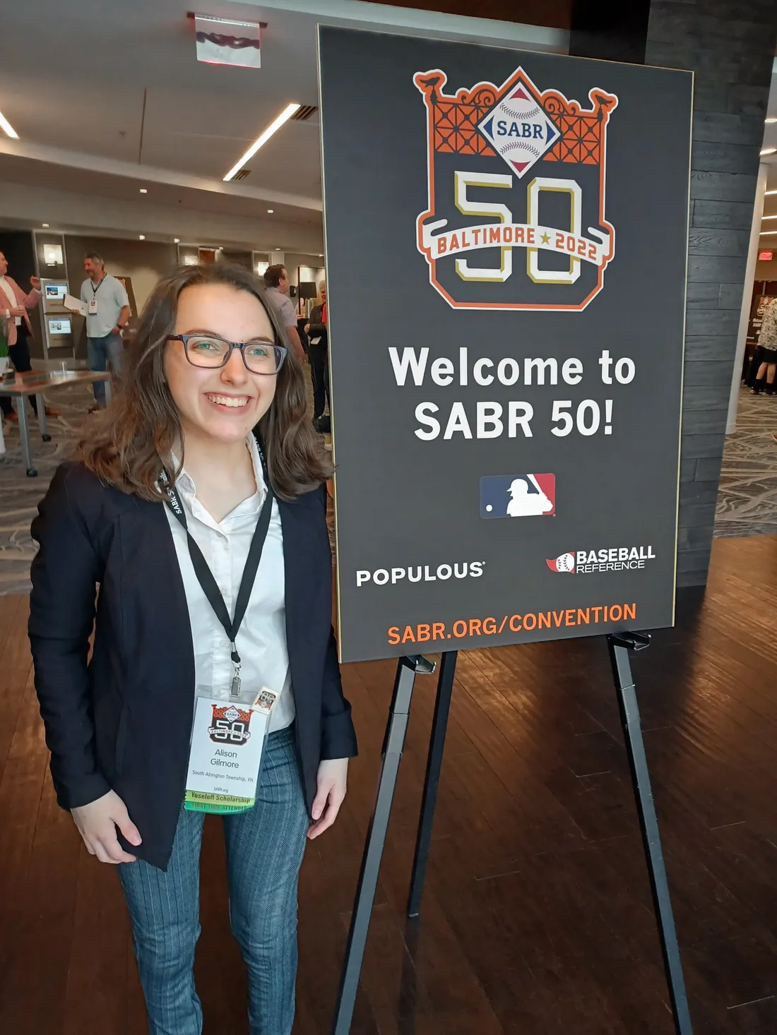 Alison Gilmore smiling in front of a welcome sign at the Society for American Baseball Research convention.