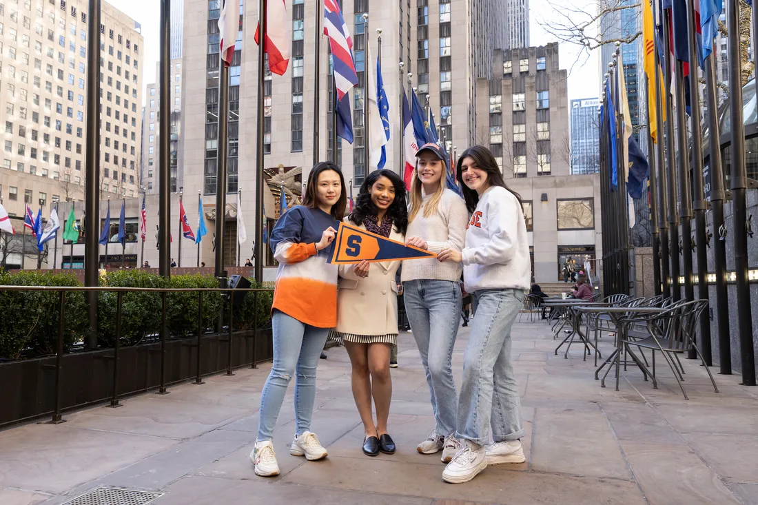 A group of people standing in NYC with a Syracuse University flag.