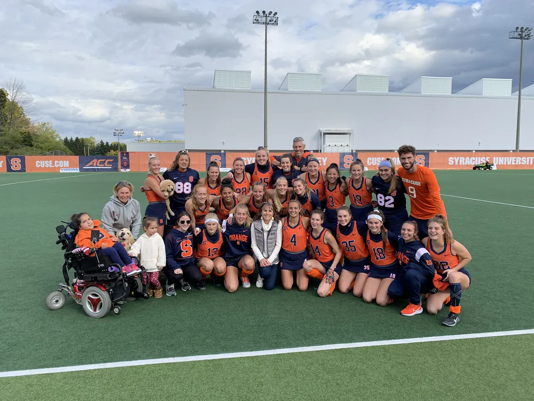 Group photo of Sullivan, her family and the Syracuse field hockey team, all dressed in Syracuse colors.