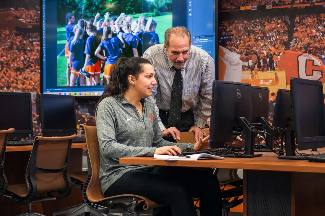 Professor helping student on computer in the the sports analysis computer lab.