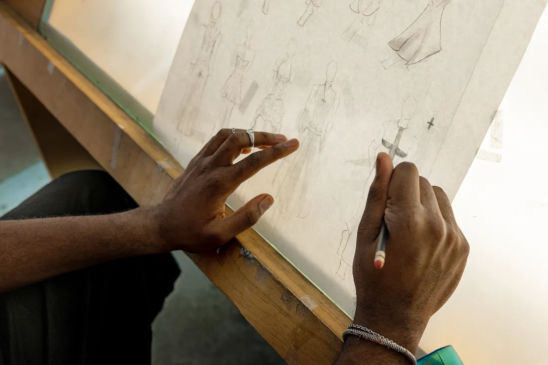 Close up photo of Williams' hands sketching designs on paper against a light box.