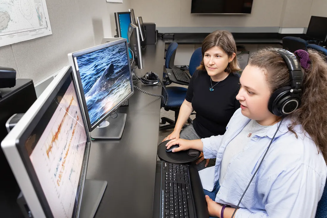 Two researchers in lab listen to audio while looking at computer monitors.