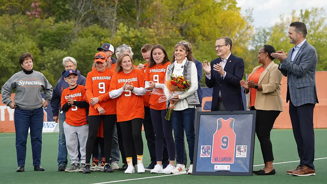 Landscape photo of a female athlete surrounded by family and friends, being celebrated on a field, flowers in her hand.