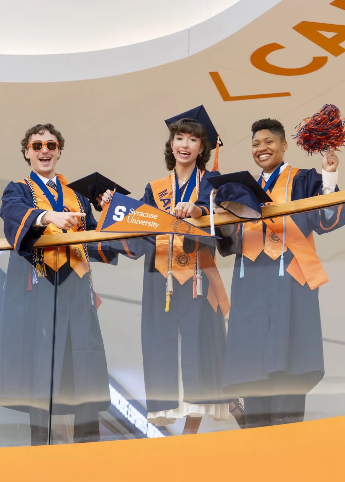 Three student marshals standing and smiling in their graduation regalia.