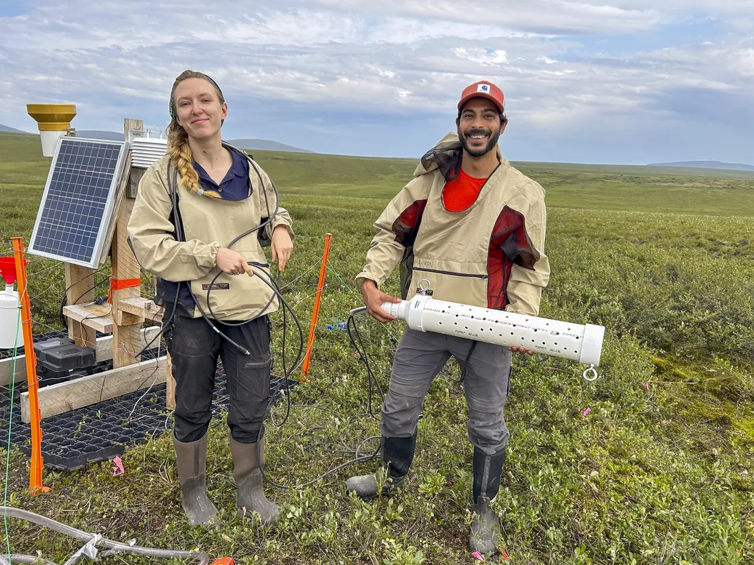 Two people standing in a field holding equipment to measure water levels in Alaska.
