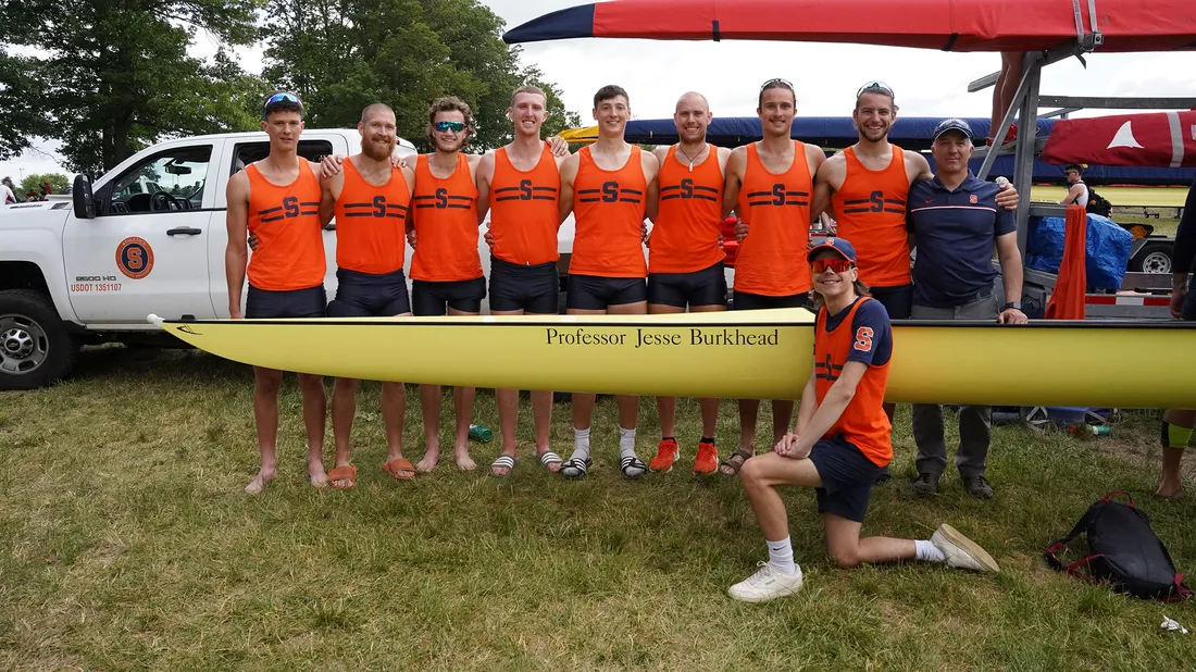 The varsity mens rowing team poses on land with their boat.