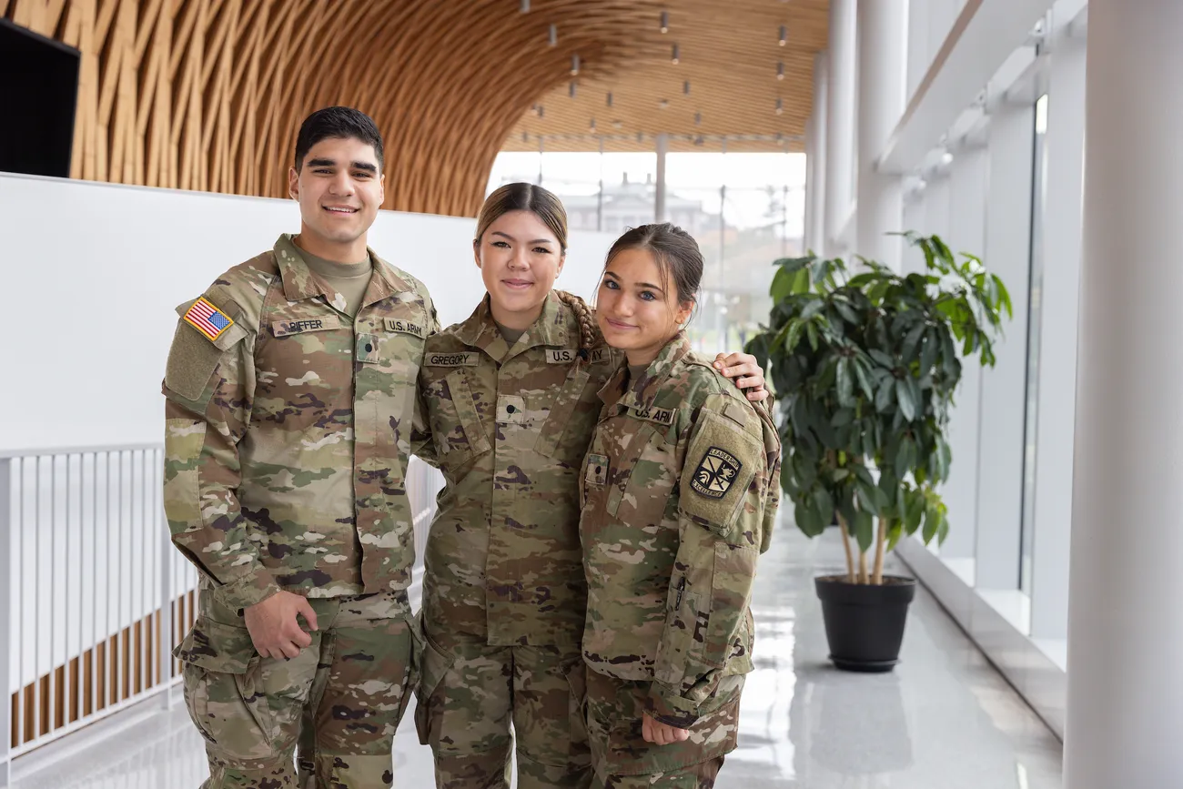 Three ROTC students standing together in a hallway smiling.