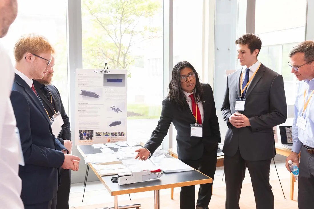 Students at presentation show invention presentation board to onlooker.