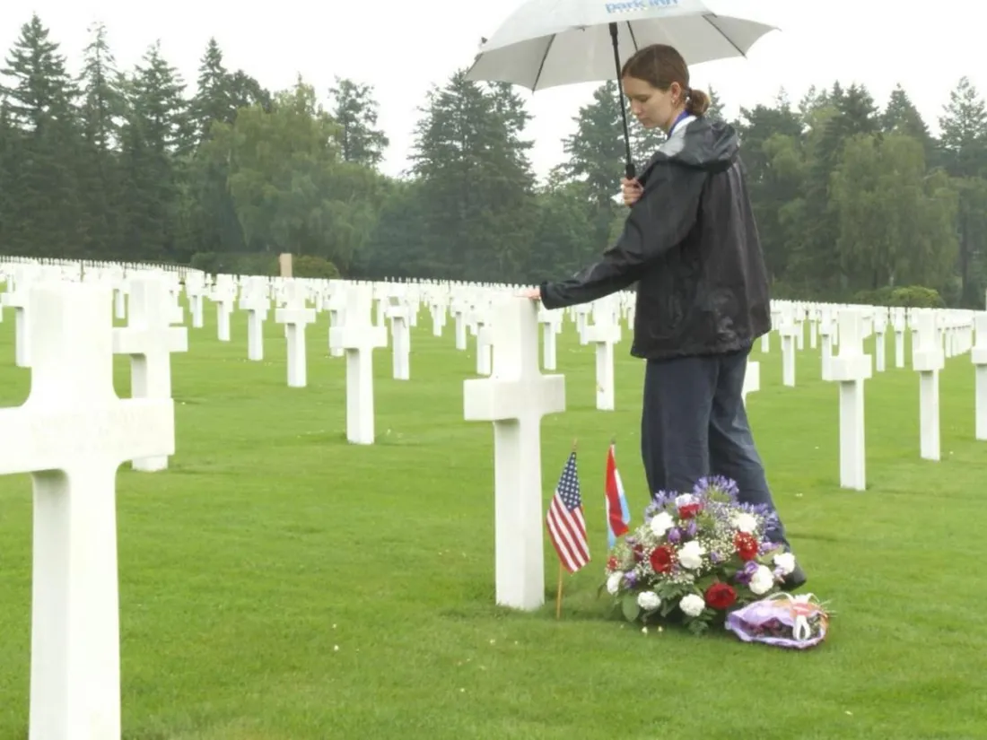Kaitlyn Kushner '26 standing at her great uncle's grave at the Luxembourg American Military Cemetery, holding an umbrella.