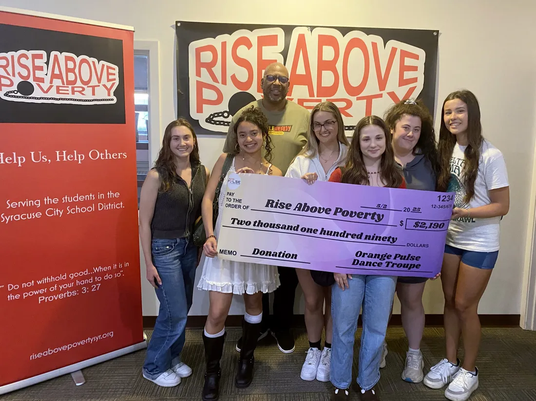 Students standing and holding a large check in front of a "Rise Above Poverty" sign.