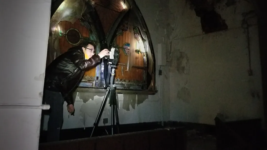 Cirasuolo in a dark church, leaning into the viewfinder of a camera on a tripod.
