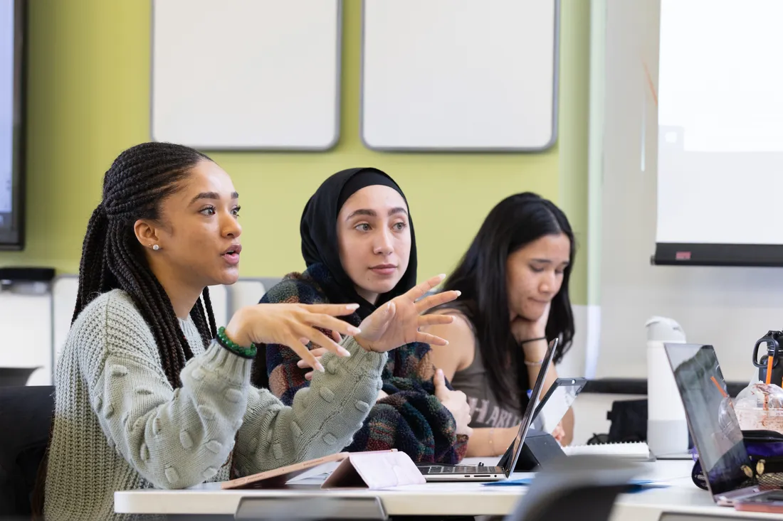 Three women talk with each other in classroom.