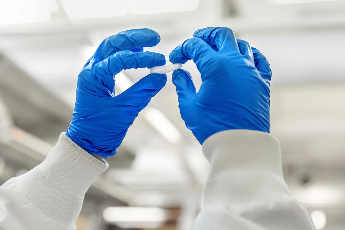 Two hands in blue gloves holding a small white object.
