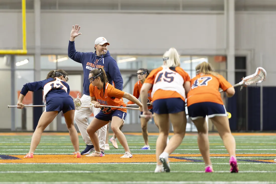 Regy Thorpe standing on the practice field alongside members of the Syracuse University women's lacrosse team.
