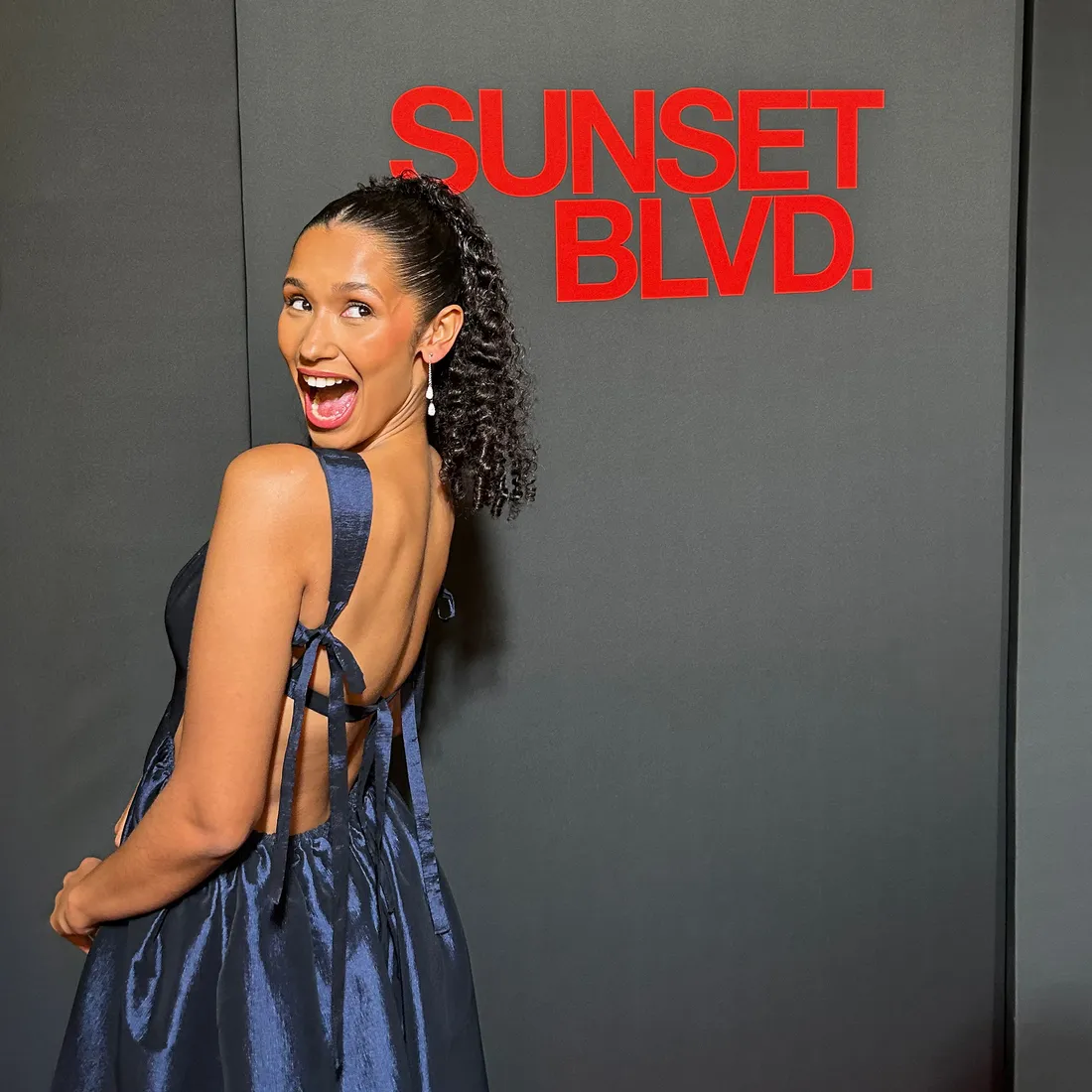 Broadway star posing in front of a wall with Sunset BLVD on it