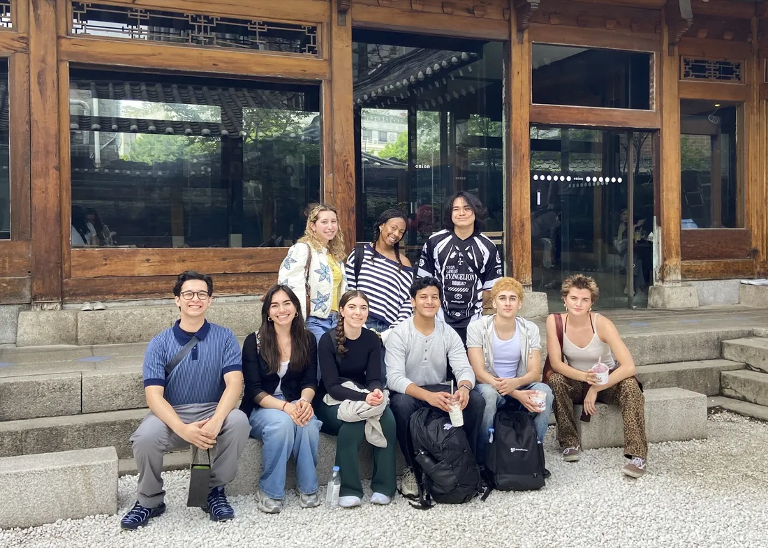 Students sitting outside of a building in Seoul, South Korea and smiling.