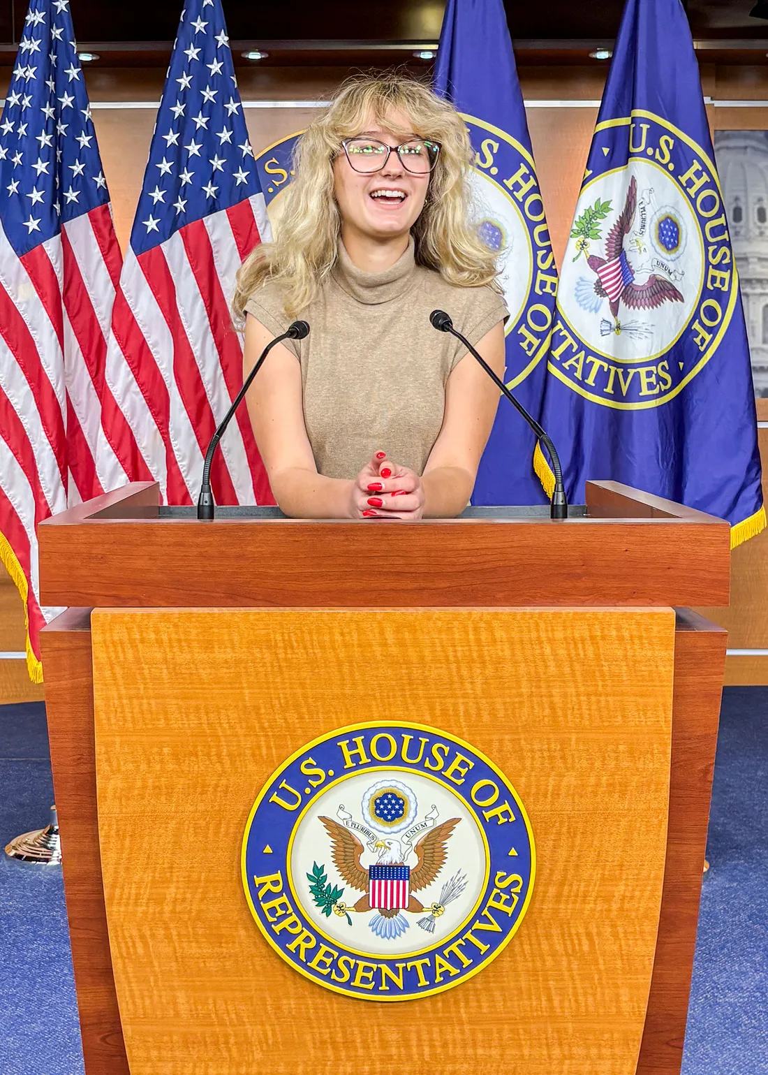 Megan Acker standing at a podium inside the press room of the house of representatives.