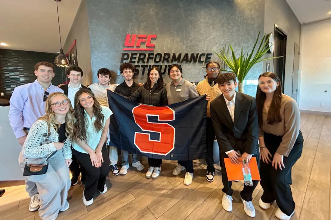 Students in the Las Vegas spring immersion program standing inside the UFC Performance Institute holding a Syracuse University flag.