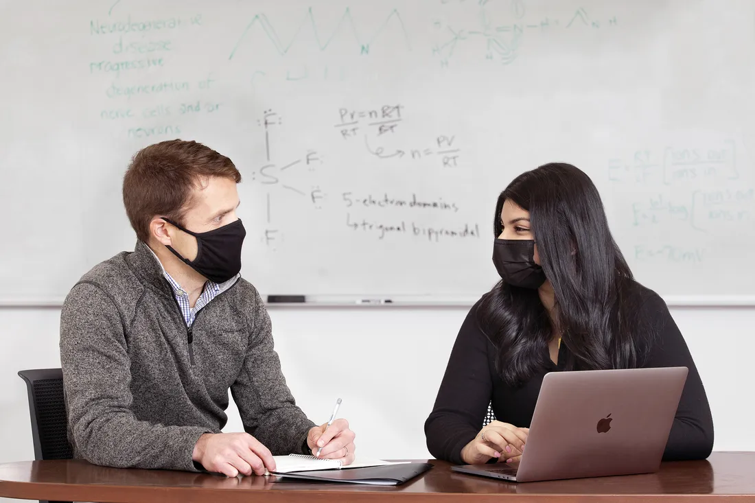 Male and female sit together at a desk with an open laptop.