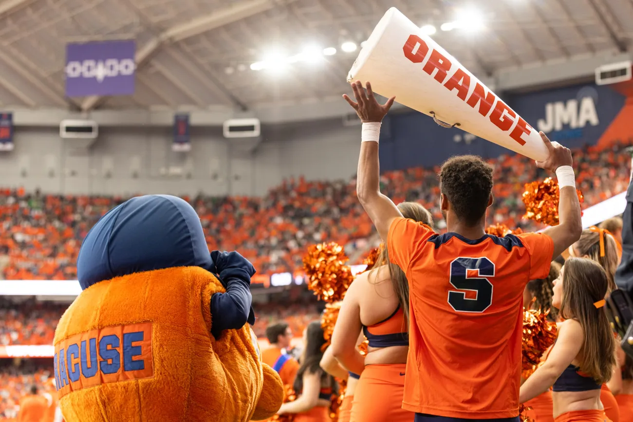 Person holding Syracuse University themed megaphone in the JMA Wireless Dome, standing next to Otto the Orange.