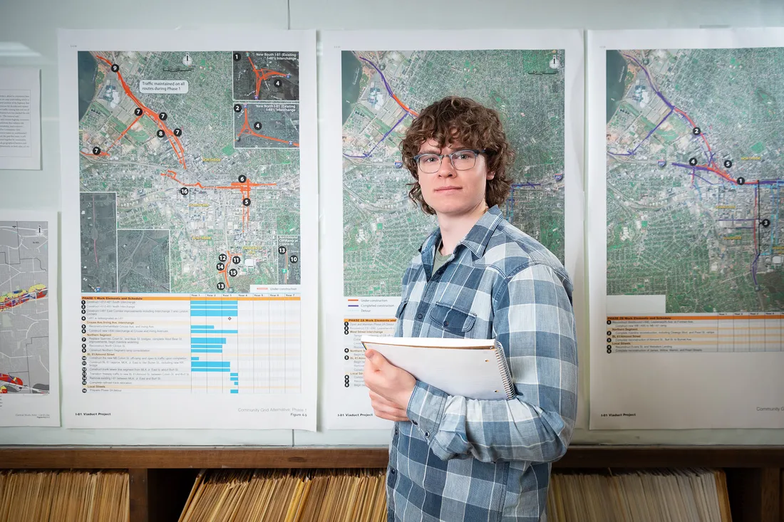 A student smiling at the camera in front of three maps