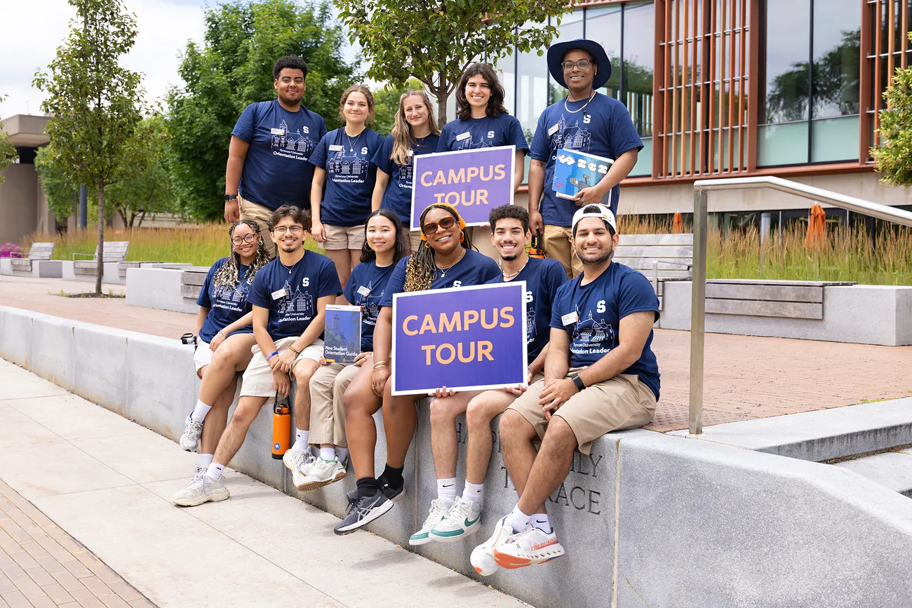 People posing for group picture while holding signs.