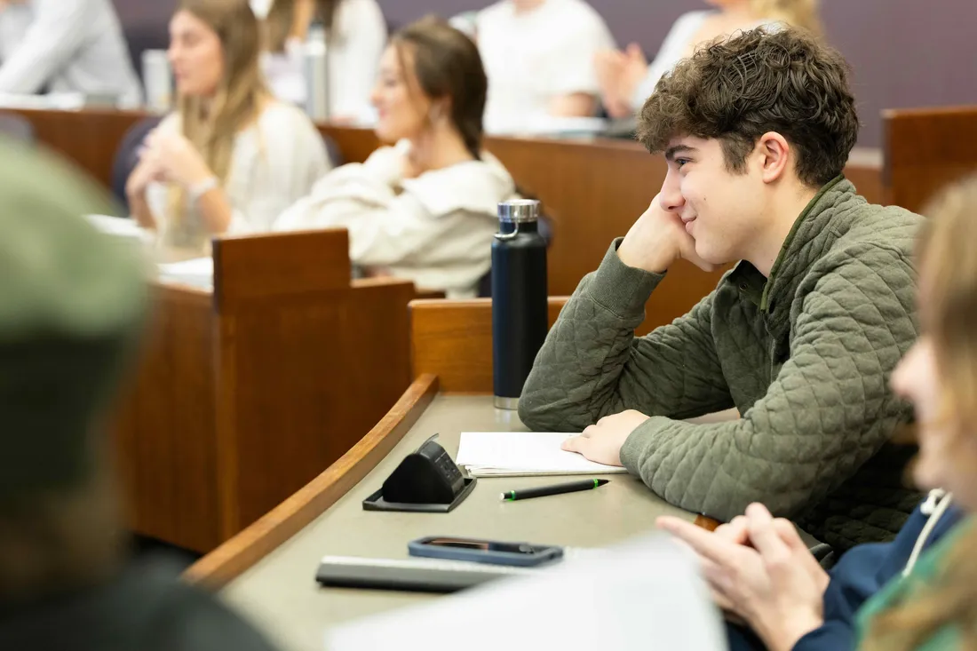 A student sitting and smiling in a Whitman School of Management classroom.
