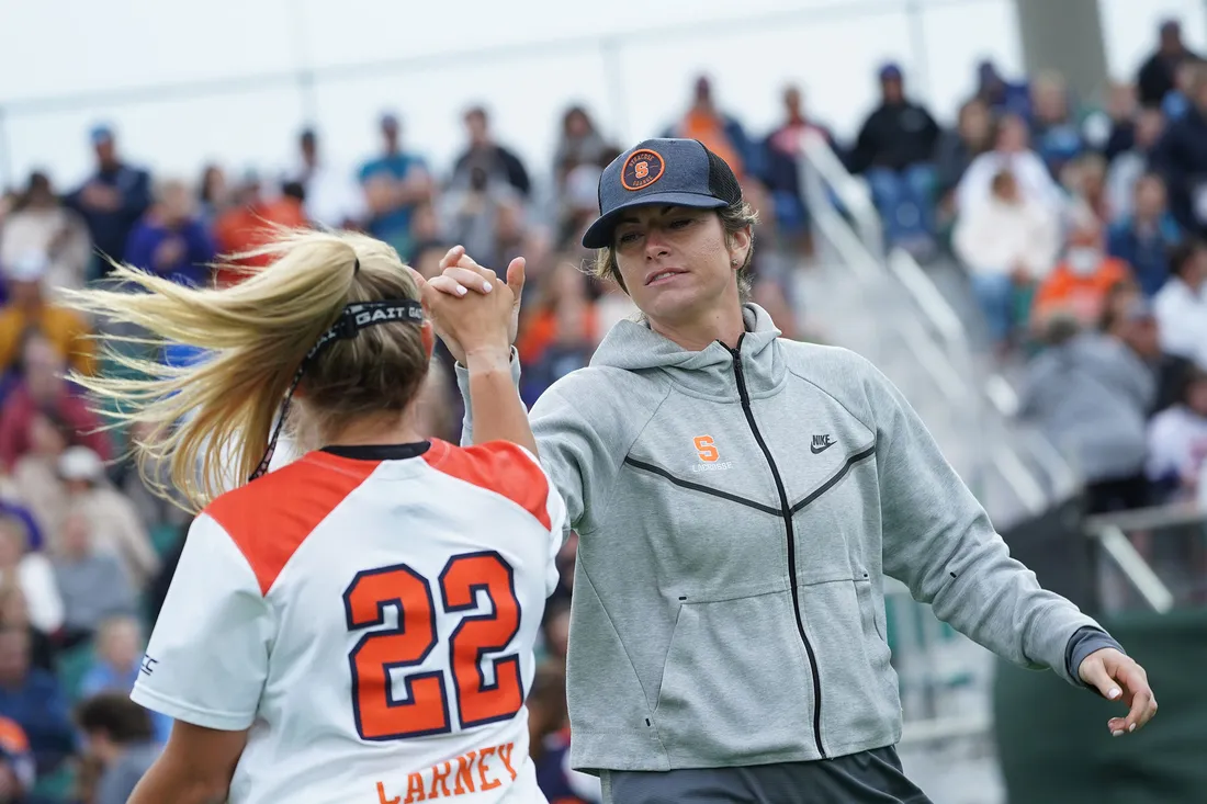 Coach high fives player on field at lacrosse game.
