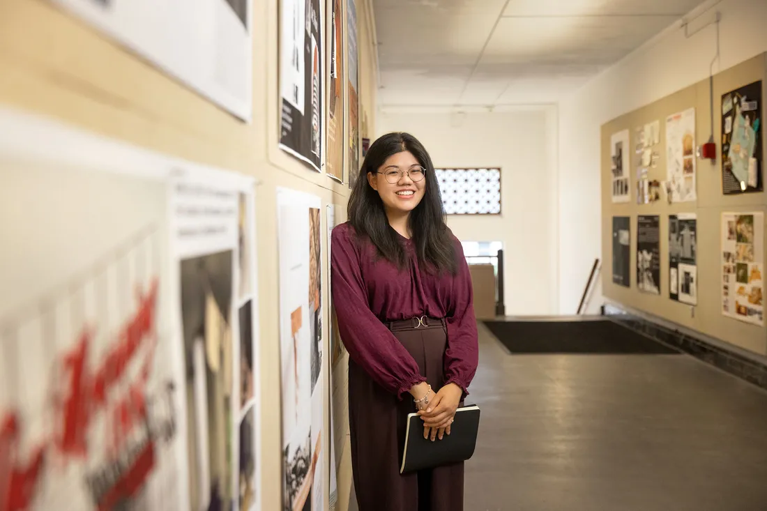 Student posing in front of artwork on the wall.