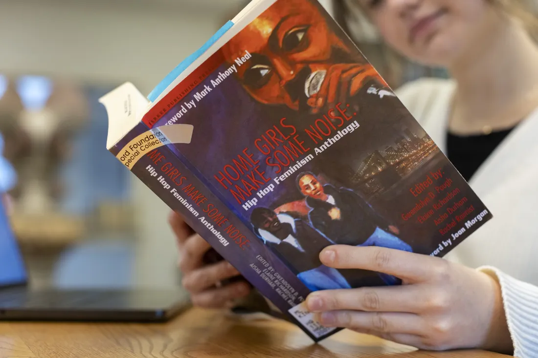 Person sitting and reading a book titled "Home Girls Make Some Noise: Hip Hop Feminism Anthology."