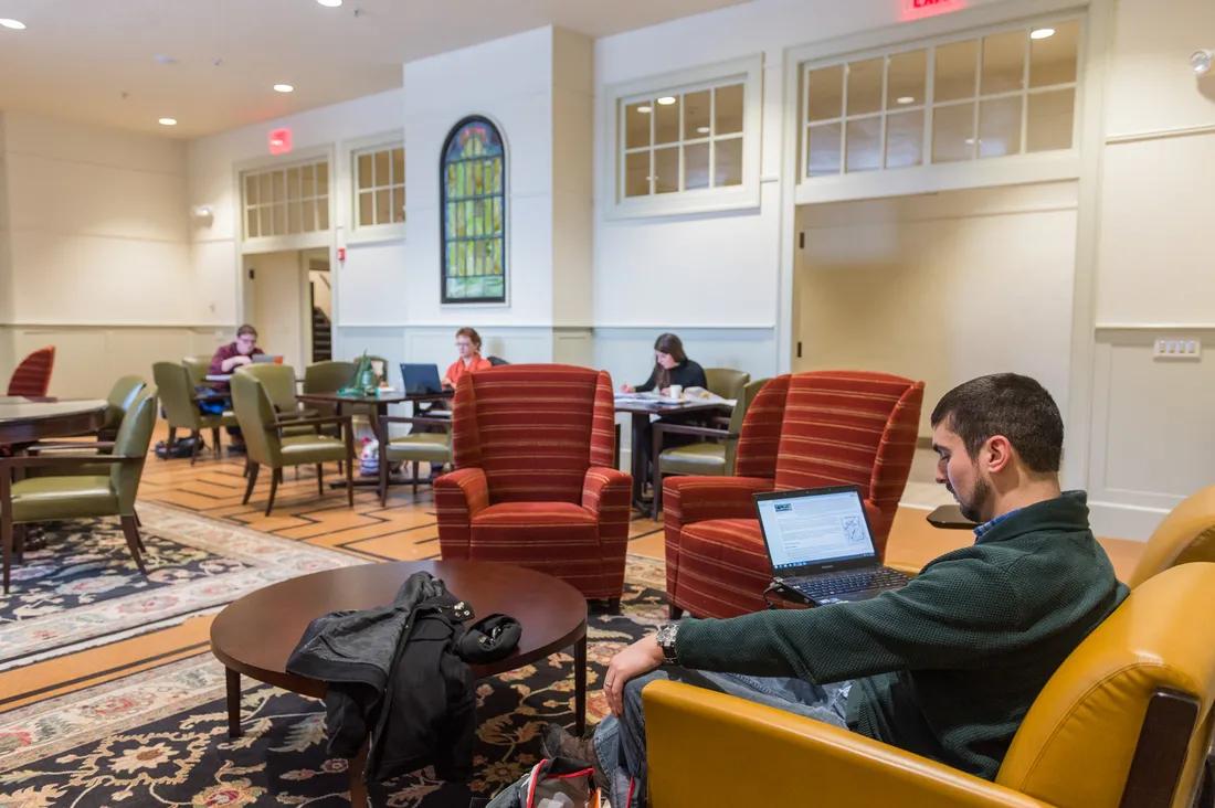 Students sitting in arm chairs studying on computers.