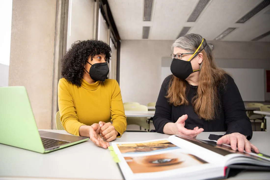 Nico Aramboles and Professor Mel White sit at a table in front of a large open book.