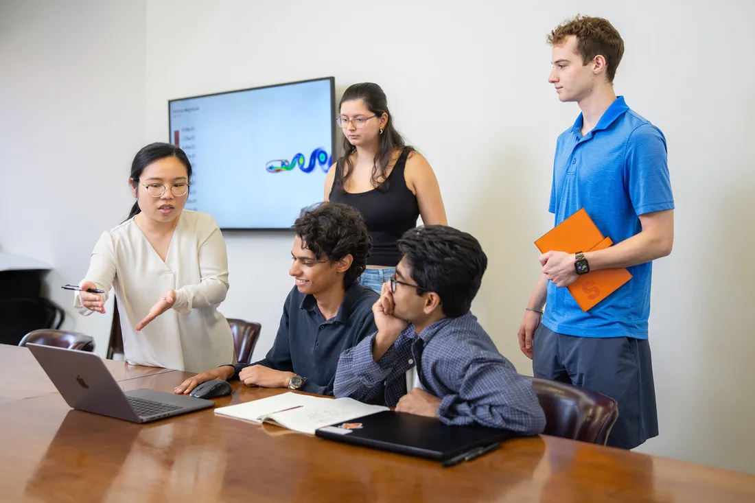 Professor Yiyang Sun pointing to a computer and speaking with undergraduate research students.