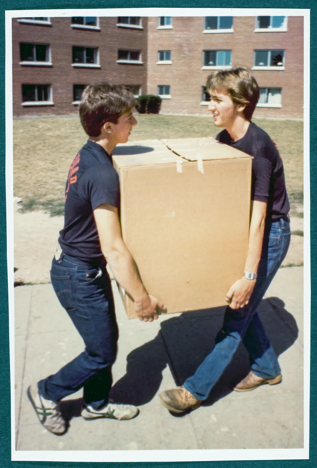Two Goon Squad workers carry boxes to dorms in 1970s