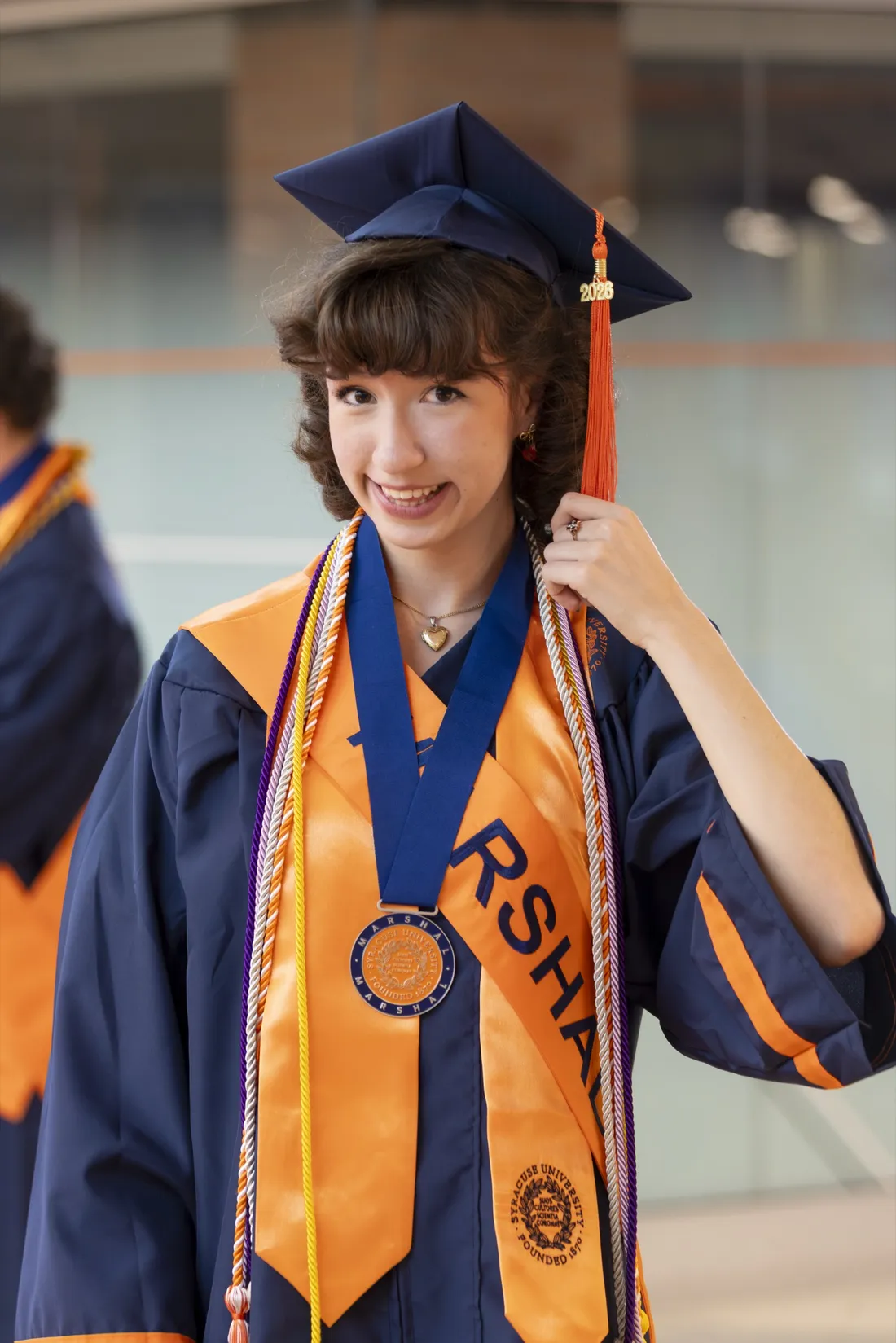 Thalia Lee '26 smiling in her graduation regalia and grabbing her tassel.