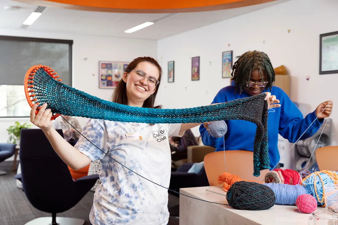 Sonja Nusser holds up scarf she is in progress of knitting.