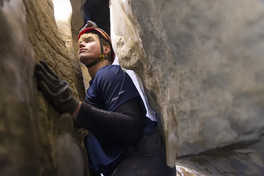 Student from Syracuse University Outing Club climbing through a narrow cave opening.