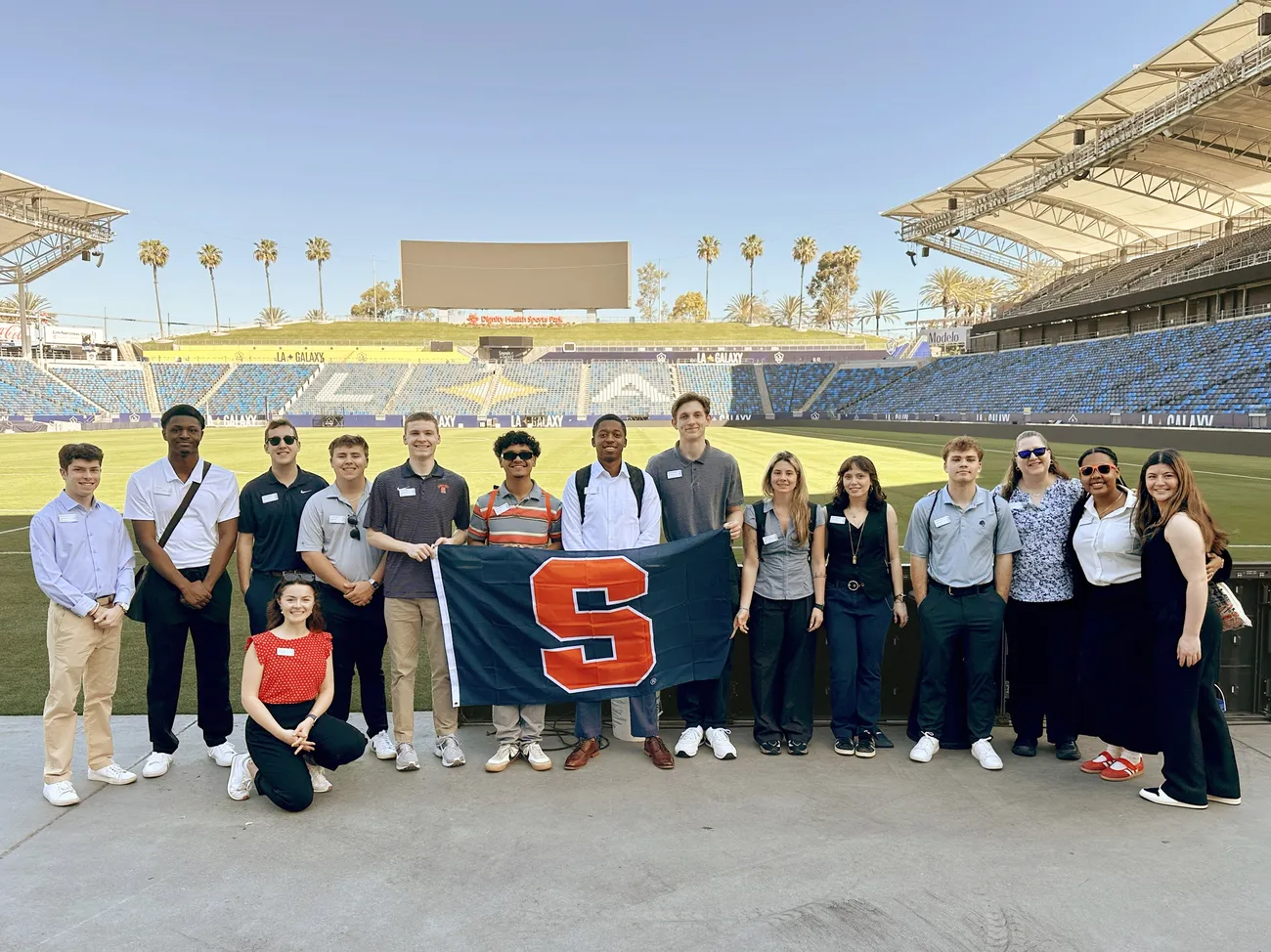 Students on an immersion trip to Los Angeles standing in the LA Galaxy stadium holding a Syracuse University flag.