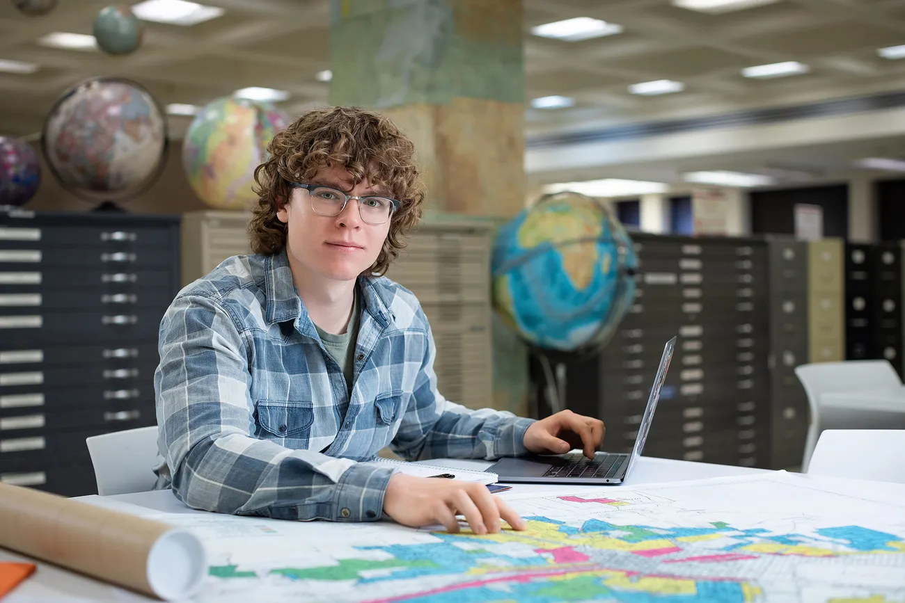 A student holding papers in front of maps