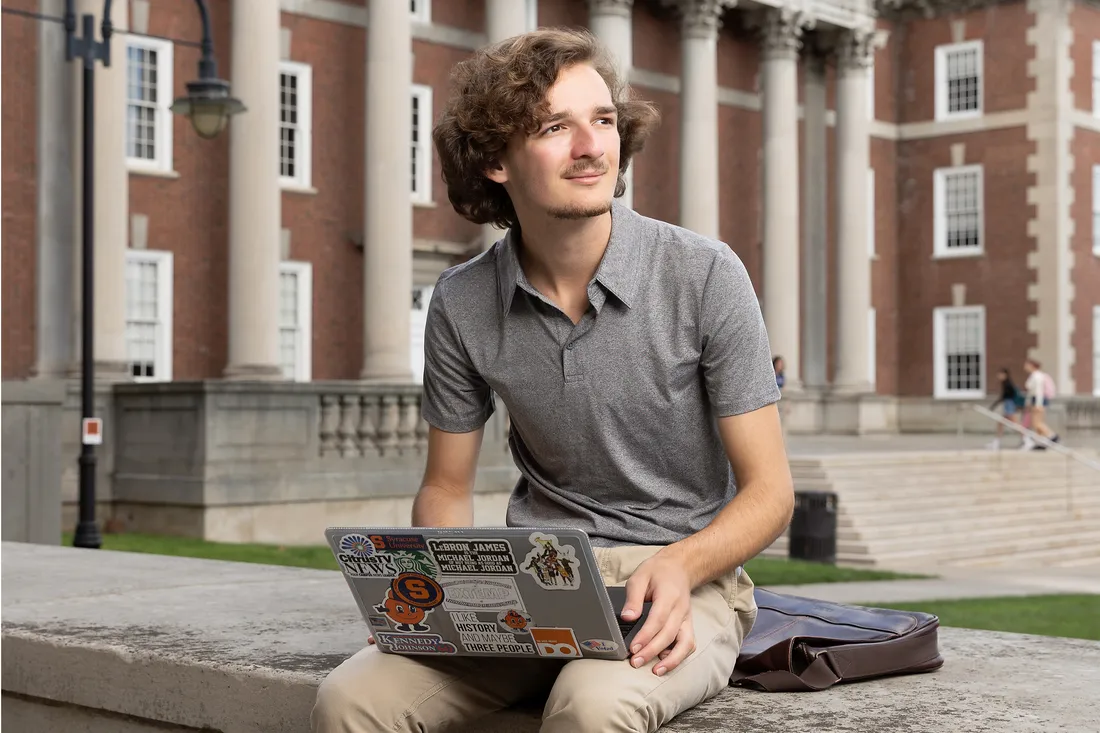 Student sits outside on campus working on computer.