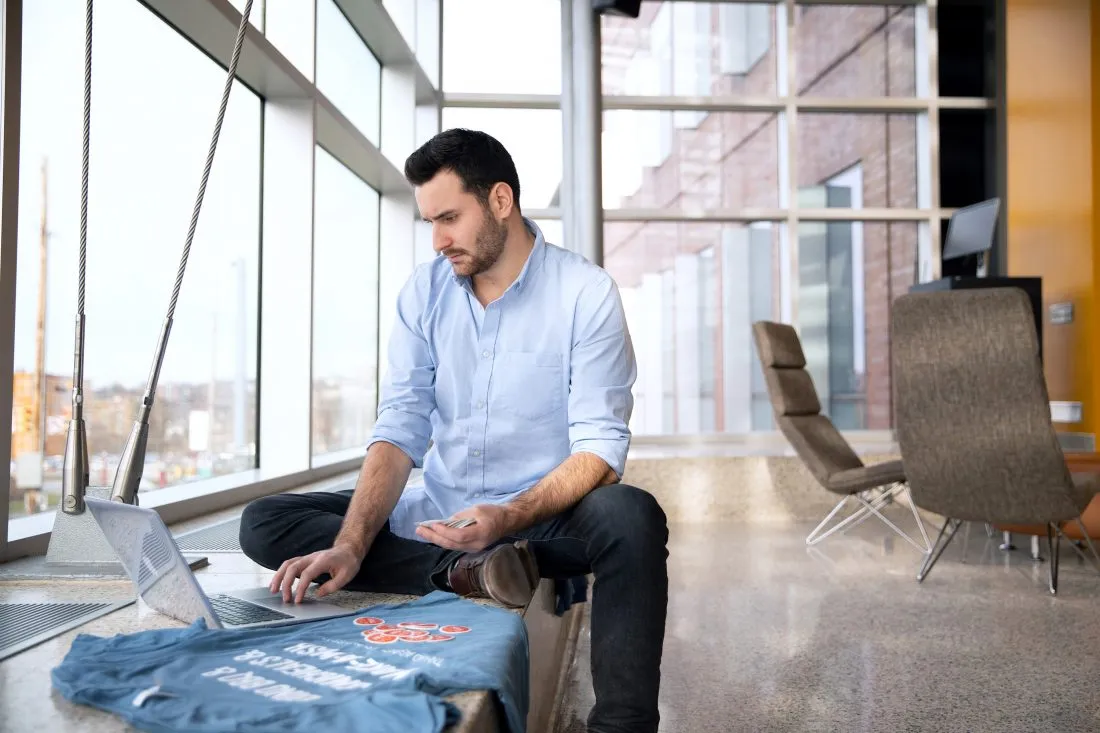 Scott Bingle uses laptop while examining stickers in a sunny atrium.